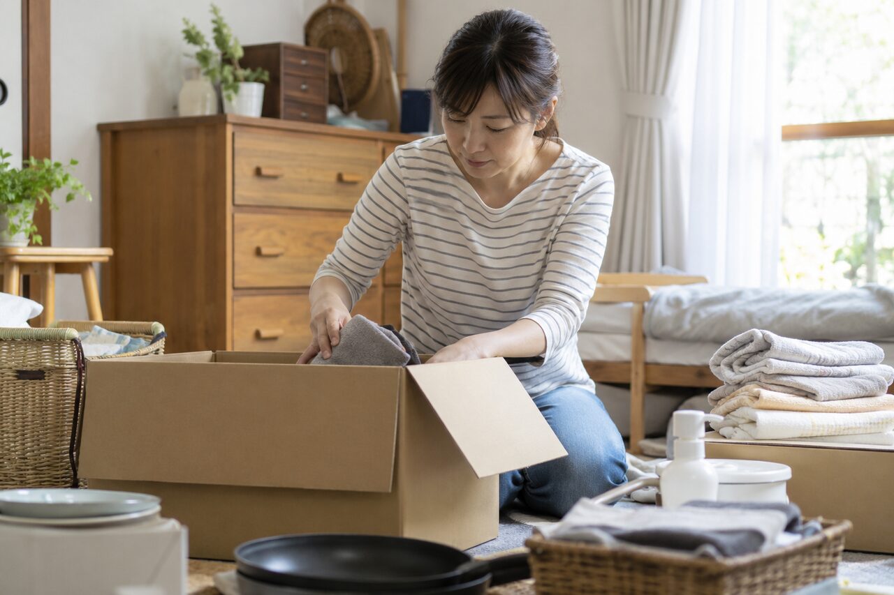 無記名の箱へ生活用品を整理する成人