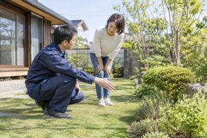 紺色の作業服の作業員が住宅の庭で芝生の状態を確認するイメージ